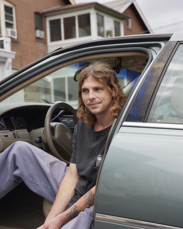 Ethan sits in the driver's seat of his green car and smiles at the camera