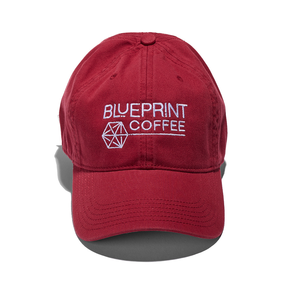 A red dad hat embroidered with the Blueprint Coffee logo in white thread across the front
