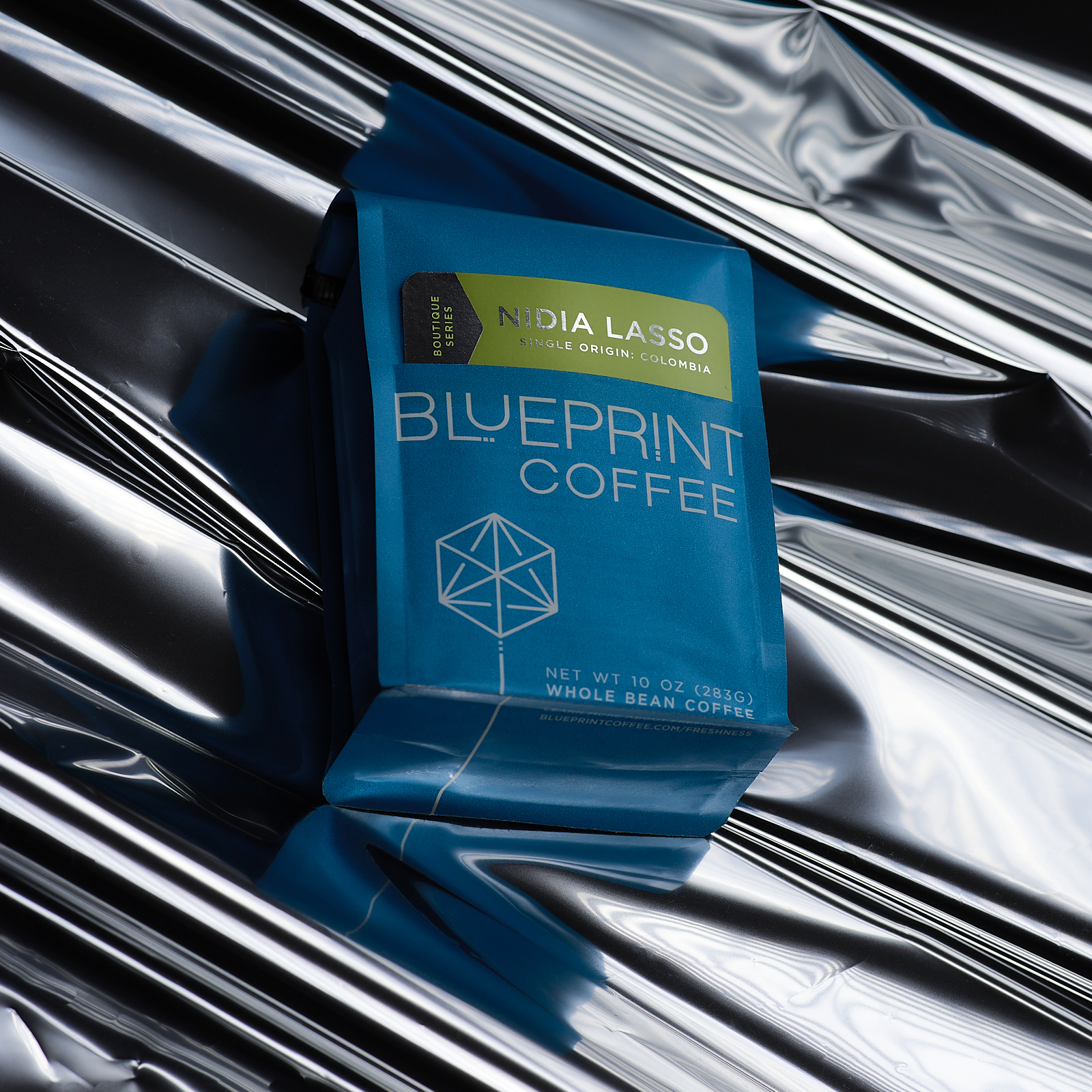 A blue bag of Nidia Lasso, Colombia roasted by Blueprint Coffee lies atop a crinkled sheet of silver metallic paper