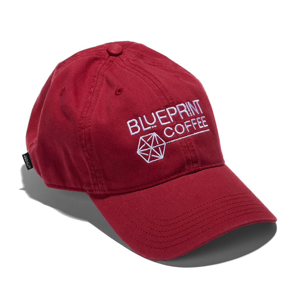 A red dad hat embroidered with the Blueprint Coffee logo in white thread across the front