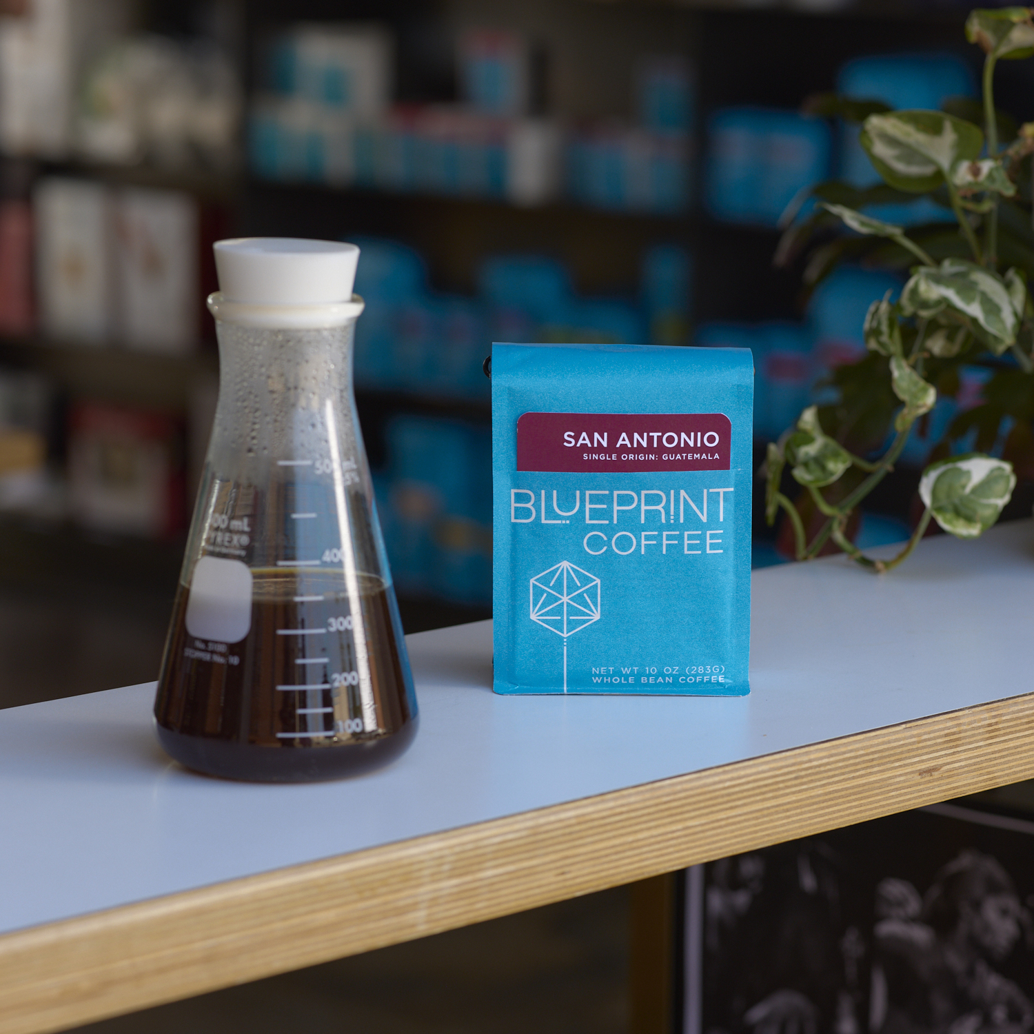 A blue bag of San Antonio, Guatemala by Blueprint Coffee sits on a white countertop bar beside an Erlenmeyer flask containing black brewed coffee